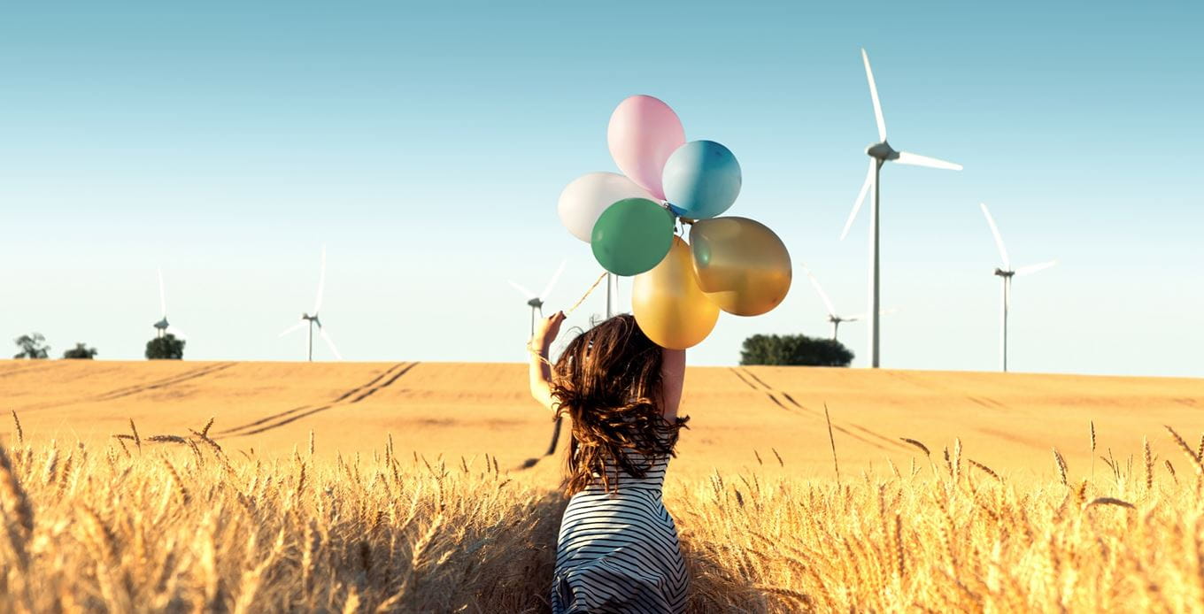 Mädchen mit Luftballons läuft durch Windmühlenfeld