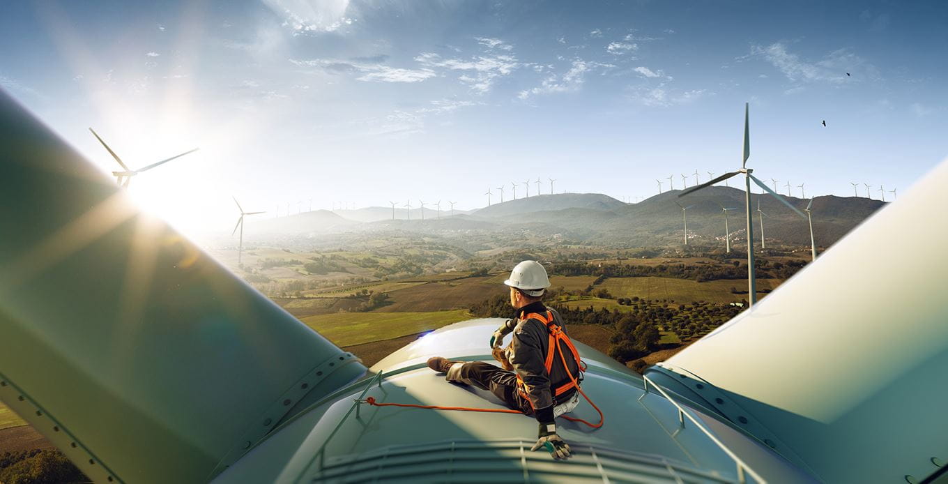 Ingenieur vor einer Windturbine in der Sonne, Blick über grüne Felder auf einen Windpark